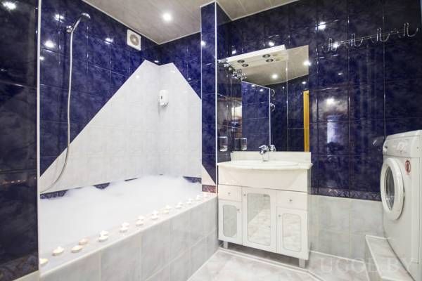 Ванна с пеной, свечи вдоль бортика, белая тумба с раковиной, зеркало с подсветкой и стиральная машина.