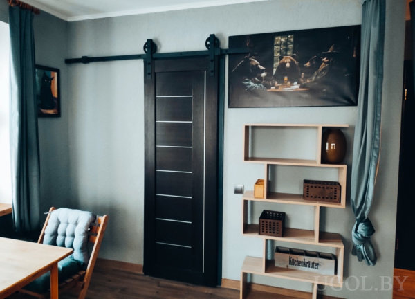 Комната с тёмной раздвижной дверью, открытым стеллажом и картиной, пародирующей «Тайную вечерю» с участием собак.