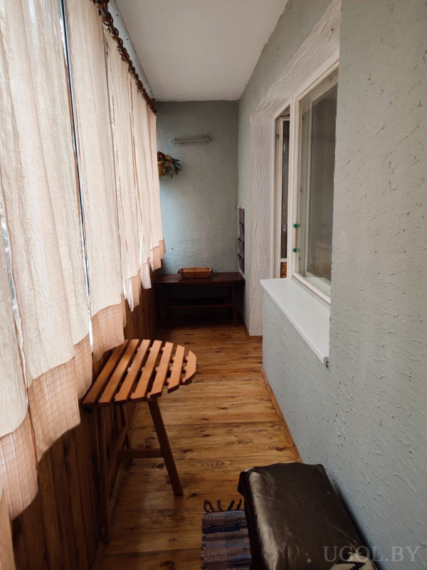 Уютный балкон с деревянным полом, складным столиком, скамьей и консолью с плетёной корзиной.