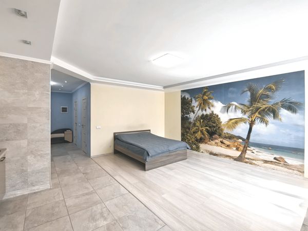 Минималистичная спальня с серым текстилем, фреской с пальмами и песком, и видом в соседнюю комнату.