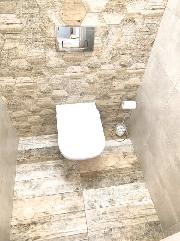 Современный туалет с гексагональной плиткой, подвесным унитазом и металлическим держателем с запасным рулоном.