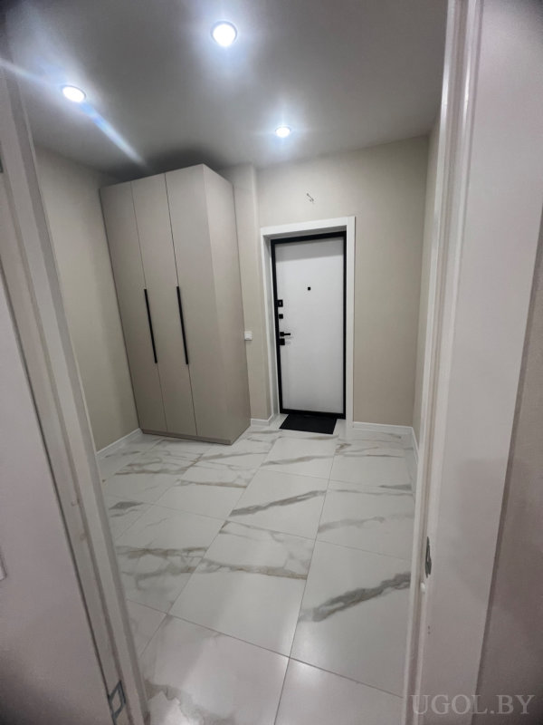 Современная прихожая с белой входной дверью, шкафом с черными ручками и мраморным полом, оформлена в нейтральных тонах.