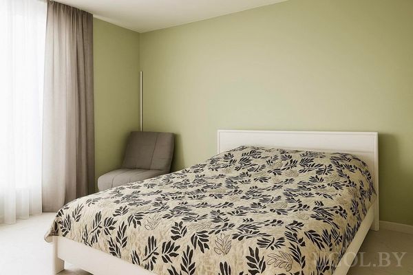 Интерьер с кроватью в листовом текстиле, зелёной стеной, серым креслом и окнами с тюлем и шторами.