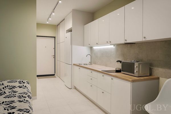 Кухонная зона с белыми шкафами, деревянной столешницей, техникой и встроенным шкафом у входной двери.