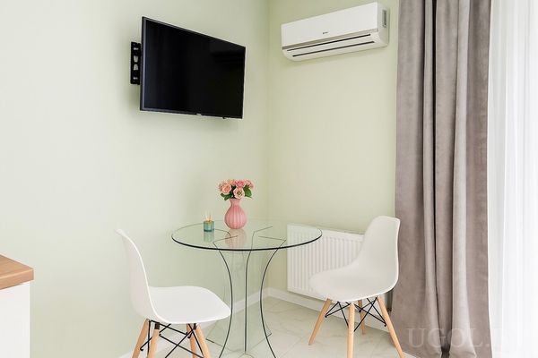 Уголок с круглым стеклянным столом, двумя стульями, вазой с цветами, телевизором и кондиционером.