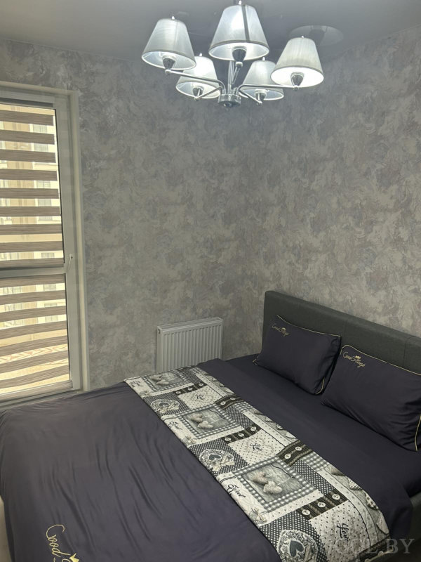 Кровать с надписью «Cozy Style» на текстиле, серые обои, люстра с абажурами и жалюзи на окне создают атмосферу уюта.