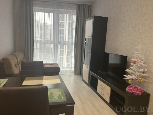 Коричневый диван, обеденная зона и ТВ-тумба с белой ёлкой, за окном — городской пейзаж с высотками.