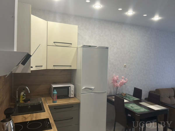 Деревянная столешница, техника и декор, включая розовые цветы на столе, создают компактное и функциональное пространство.