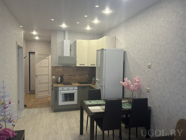 Белая и серая мебель, деревянный фартук, два декоративных дерева — розовое и белое — на фоне светлых стен и пола.