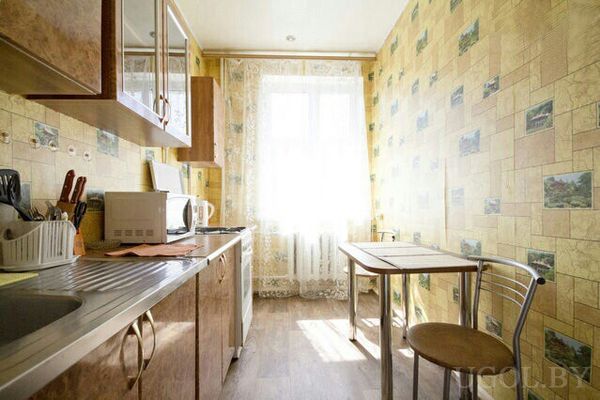 Компактная кухня с мойкой, микроволновкой, чайником, шкафами и небольшим столом с двумя стульями.