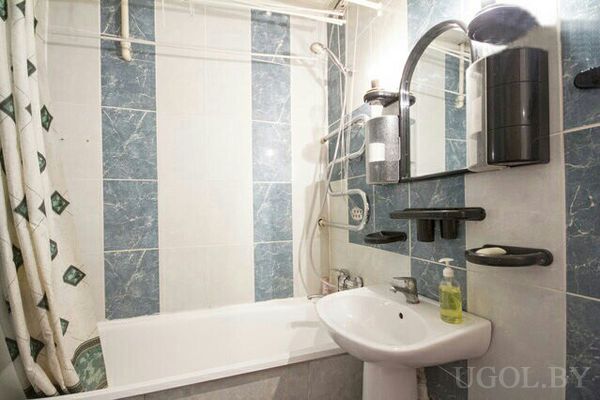 Небольшая ванная с белой ванной, душем, умывальником, зеркалом и сине‑белой плиткой.