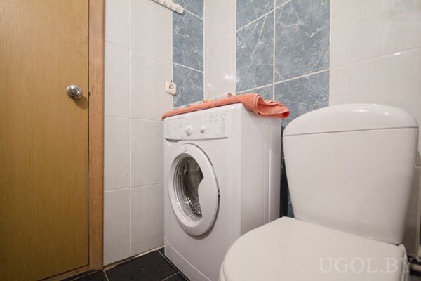 Компактный санузел с белой стиральной машиной, розовым полотенцем и унитазом.