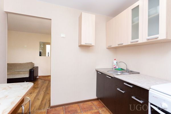 Кухня с белыми верхними шкафами и тёмными нижними, мойкой и диваном в соседней комнате.