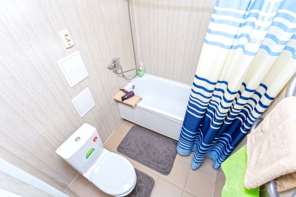 Компактная ванная с белым унитазом, ванной, душем и голубой полосатой шторкой.