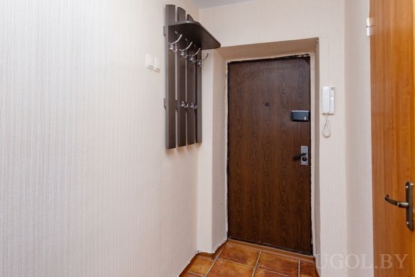 Небольшая прихожая с деревянной входной дверью, домофоном и вешалкой для одежды.