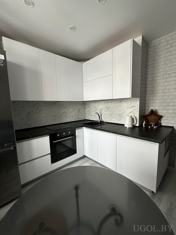 Интерьер с белыми шкафами, мраморным фартуком, чёрной мойкой, плитой и кирпичной отделкой стен.