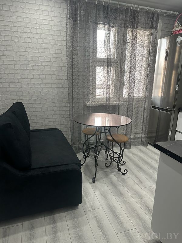 Комната с диваном, столом с отражающей поверхностью, табуретами и окнами с узорчатым тюлем.