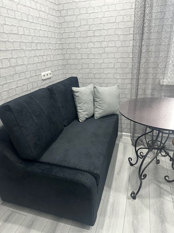 Компактная зона с диваном, столом на кованых ножках, белой розеткой и кирпичной отделкой стен.
