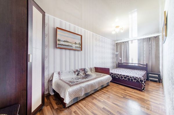 Комната с кроватью, диваном, шкафом, торшером, картиной и окнами с тюлем и плотными шторами.