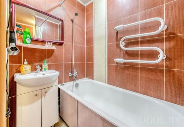 Комната с умывальником, зеркалом, полками с косметикой, плиткой в красно-бежевых тонах и душем.