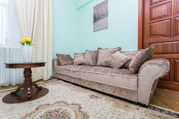 Гостиная с бежевым диваном, круглым столиком с жёлтыми тюльпанами, ковром с узором и фотографией на стене.