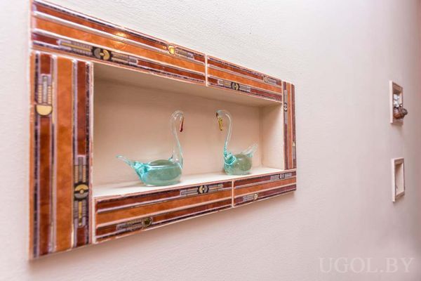 Стена с декоративной нишей, украшенной плиткой, и двумя стеклянными фигурками лебедей.