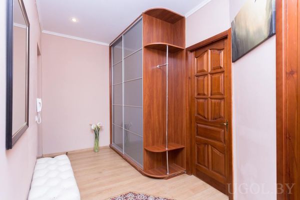 Светлая прихожая с зеркальным шкафом‑купе, мягкой скамьёй, вазой с цветами и межкомнатной дверью.