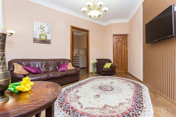 Светлая гостиная с кожаными диванами, ковром с узором, журнальным столиком с жёлтыми тюльпанами и телевизором.