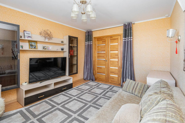 Светлый диван, ковёр, ТВ на тумбе, полки с декором, витрина, две деревянные двери и шторы с контрастом.