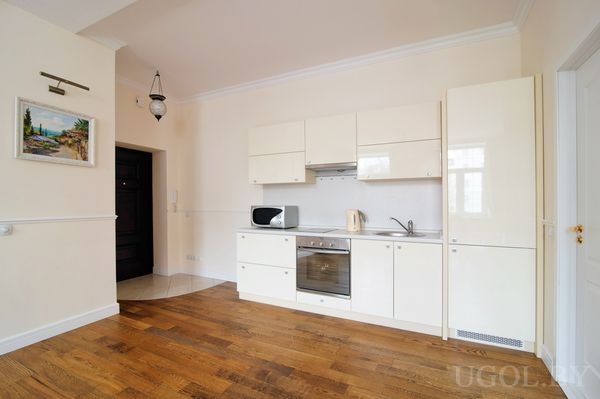 Белые шкафы без ручек, встроенная техника и картина с пейзажем под подсветкой. Тёплый свет и отражения на глянцевых фасадах усиливают ощущение простора.