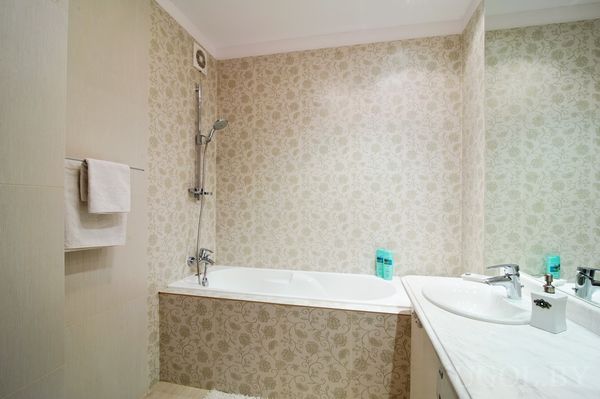 Угловая ванна с душем, белая раковина с зеркалом и настольными аксессуарами. Обои с цветочным узором добавляют мягкости и уюта.