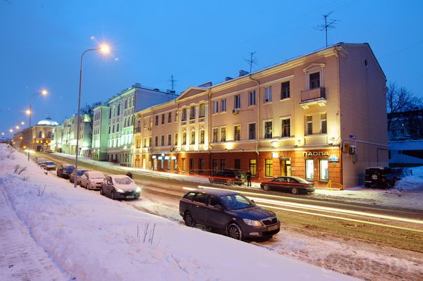 Снежная дорога с машинами и классическими фасадами. Световые следы от фар и вывеска «ПАПА» подчёркивают динамику и вечернюю жизнь города.