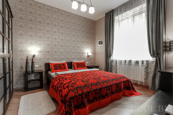 Современная спальня с двуспальной кроватью, красно‑чёрным покрывалом с цветочным узором, прикроватными тумбочками и шкафом с зеркальными дверцами.