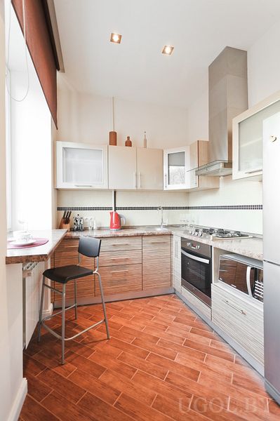 Компактная кухня с угловым гарнитуром, плитой, вытяжкой, микроволновкой и красным электрочайником.