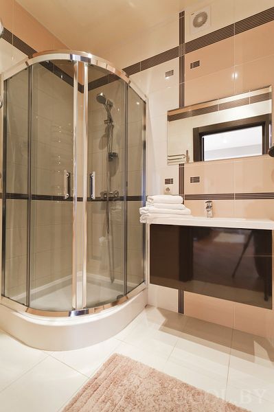 Современная ванная с душевой кабиной, белой тумбой с раковиной, зеркалом и сложенными полотенцами.