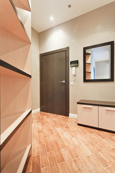 Современная прихожая с тёмной входной дверью, высоким стеллажом, зеркалом и тумбой для обуви.