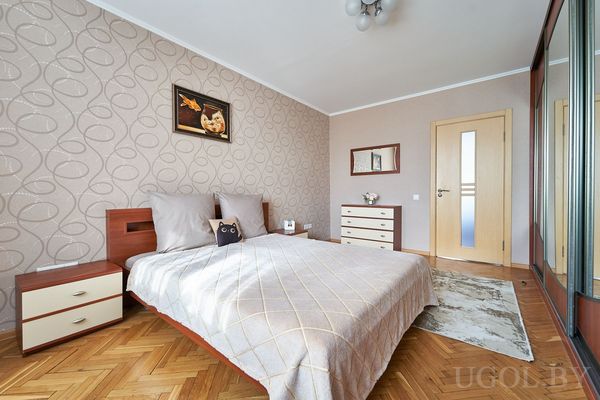 Комната с кроватью в светлом текстиле, картиной над изголовьем и зеркальным шкафом вдоль стены.