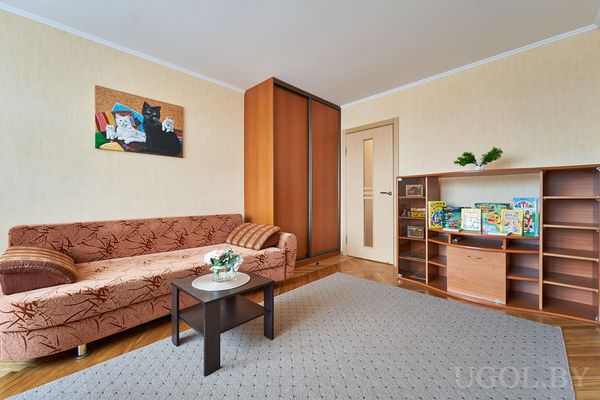 Комната с коричневым диваном, журнальным столиком, ковром и книжной полкой с детскими книгами.