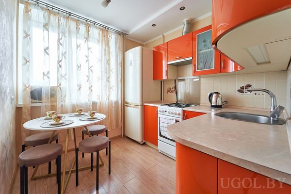 Компактная кухня с яркими фасадами, плитой, холодильником и круглым столом с сервировкой.