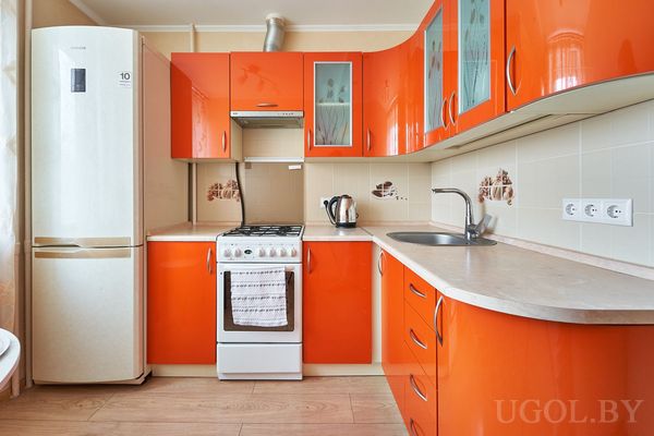 Кухня с оранжевыми фасадами, плитой, холодильником и декоративной плиткой на фартуке.
