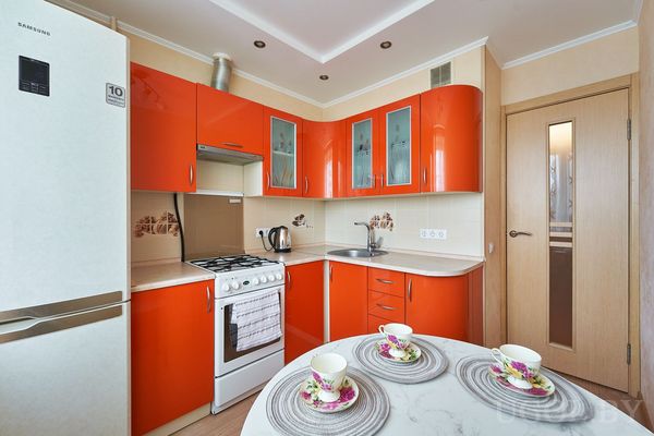 Кухня с фасадами в красно-оранжевых тонах, плитой, холодильником Samsung и круглым столом.