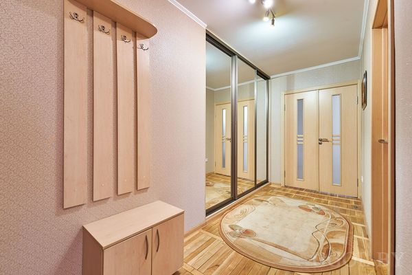 Светлая прихожая с деревянной вешалкой, зеркальным шкафом и ковром на полу.