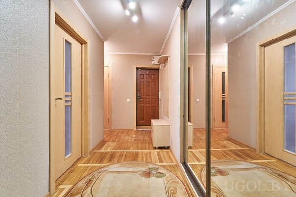 Современный коридор с зеркальным шкафом, круглым ковром и светлыми дверями с матовым стеклом.