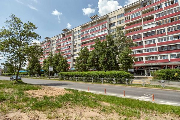 Жилой дом с фасадом в красно-белых тонах, балконами и деревьями вдоль дороги.