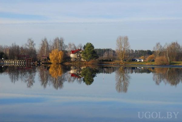 Спокойное озеро с отражением дома с красной крышей и осенних деревьев.