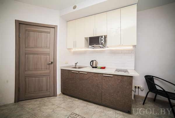 Небольшая кухня с белыми верхними шкафами, коричневыми нижними, мойкой, плитой и микроволновкой.