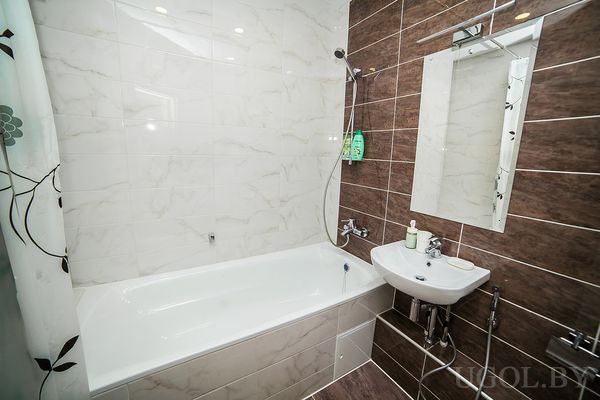 Современная ванная с белой ванной, раковиной, зеркалом и плиткой под мрамор и дерево.