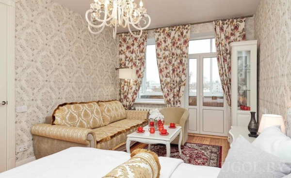 Бежево-золотая мебель, красный чайный сервиз на белом столе и цветочные элементы в интерьере.