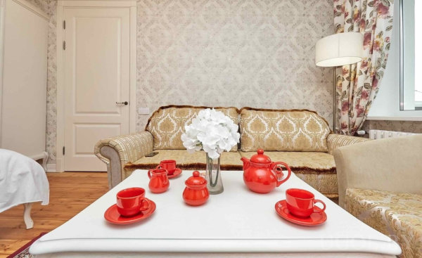 Белый стол с ярким чайным сервизом, винтажный диван и цветочные шторы в светлой комнате.