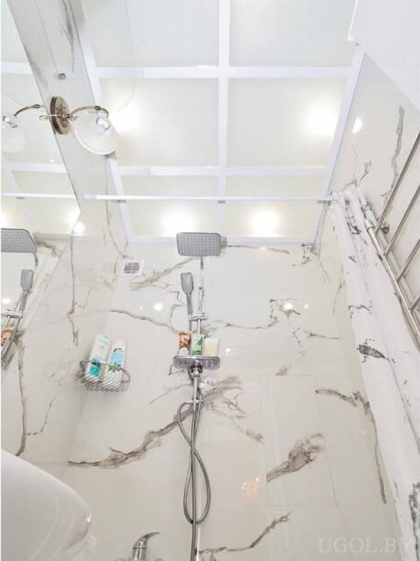Квадратный верхний душ, настенный светильник и металлическая полка с косметикой на фоне мрамора.